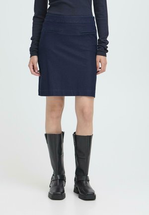 Dark denim skirt with a fitted design, two front pockets, overlaid seams, and a clean hem. Paired with knee-high black leather boots.