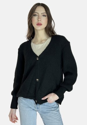 Cardigan nero a maglia con scollo a V, bottoni frontali e vestibilità rilassata. Presenta un tessuto testurizzato e maniche lunghe. Indossato sopra una maglietta leggera.