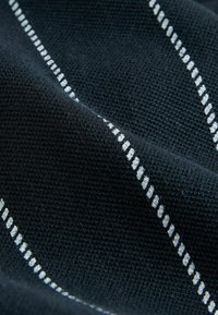Zwarte stof met een gestructureerde weving, voorzien van diagonale witte strepen en verspreide witte stikselaccenten.