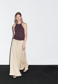 Dark brown fitted tank top paired with a flowing beige maxi skirt. The skirt features a textured fabric and a wide, loose fit.