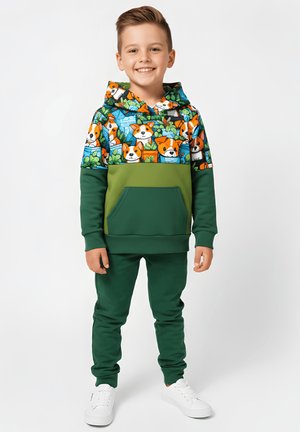 Zielony komplet z bluzy z kapturem i spodni. Bluza z nadrukiem wielokolorowych psów i kieszenią kangurka; gładka faktura. Dopełnieniem stroju są białe trampki.