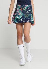 Gonna sportiva blu navy con un vivace motivo floreale, design plissettato, dettagli bianchi e una cintura comoda. Indossata con calze bianche e sneakers.