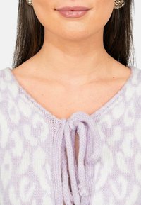 Maglione lavorato a maglia di colore lilla con una stampa leopardata bianca testurizzata, caratterizzato da un scollo a V e una chiusura con nodo frontale. Superficie morbida e pelosa.