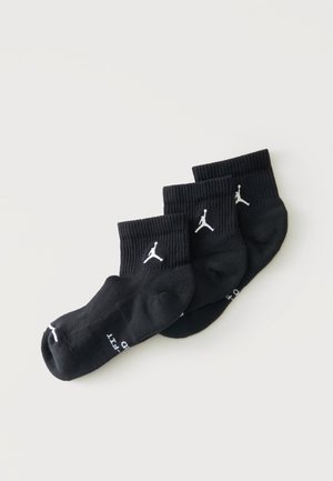 Trzy pary czarnych skarpetek za kostkę z białymi logo Jumpman ułożonych na jasnym tle.