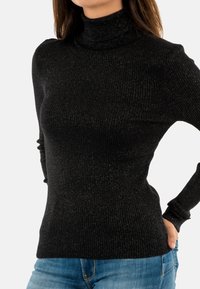 Maglione a collo alto nero a coste con un design aderente, caratterizzato da una leggera lucentezza e maniche lunghe, abbinato a jeans blu.