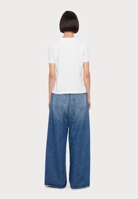 Vit bomullst-shirt med korta ärmar kombinerad med löst sittande, ljusblå denimjeans med vida ben, som har två bakfickor och blekta områden.