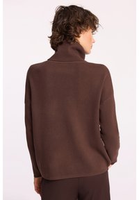 Brązowy sweter z golfem wykonany z miękkiego materiału, o luźnym kroju i długich rękawach, z gładką teksturą i prążkowanym wykończeniem.