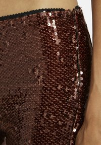 Bruine paillettenbroek met een aansluitend ontwerp. Heeft een zijrits en een gegolfde zwarte tailleband. De textuur is glad en glanzend.