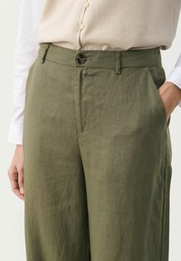 Pantaloni di lino leggeri, verde oliva, con una texture liscia, dotati di chiusura a bottone, passanti per la cintura e tasche laterali.