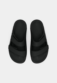 Sorte sandaler i svart med en teksturert overflate, utstyrt med to justerbare stropper og en formet såle. Glatt finish, minimalistisk design.