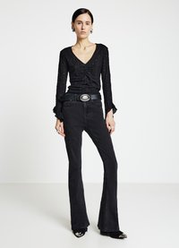 Haut à manches longues noir texturé avec un col en V, associé à un jean noir évasé taille haute et des chaussures à talons pointues noires. Boucle de ceinture argentée.