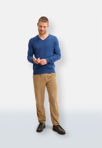 Blauer V-Ausschnitt-Pullover aus weicher Wolle, kombiniert mit hellbraunen Cordhosen und dunkelbraunen Schuhen. Das Outfit hat eine lässige Passform.