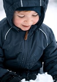 Marinblå vinterjacka med huva, texturerat tyg, med vita detaljer och ett dragkedjefäste i trä. Snöflingor syns på ytan.