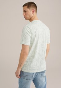 Camiseta verde claro con un patrón circular, cuello redondo, mangas cortas y un corte relajado. Combinada con jeans de mezclilla azul claro.