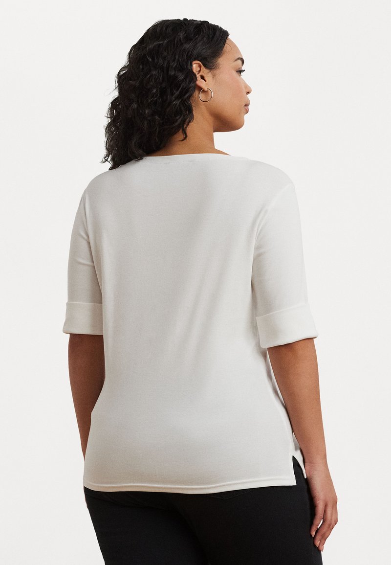 Λευκή μπλούζα κοντομάνικη με λεπτομέρειες σε ρολό, στρογγυλή λαιμόκοψη και πλαϊνές σχισμές, φτιαγμένη από ένα μαλακό ύφασμα με ελαφριά ελαστικότητα.