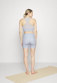 Conjunto de top desportivo e calções azuis claros com um padrão floral. O material é elástico. As costas têm um design estilo corredor. Descalça em um tapete de yoga.