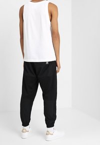 Vit bomullstanktop, svarta joggers med texturerad tyg, åtsittande manschetter och sidostäpplar, parat med vita sneakers med guldaccenter.