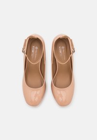 Ballerines plates en cuir verni couleur nude avec un bout arrondi et une bride de cheville ornée d'une boucle argentée. Surface lisse avec une finition brillante.
