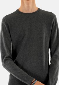Pull en tricot gris avec des manches longues et un col rond. Texture douce, design ajusté, et poignets et ourlet côtelés. Accentué par un bracelet au poignet.