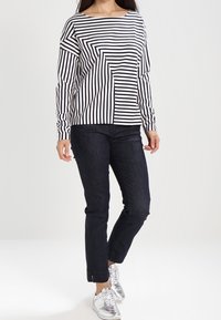 Top de manga larga con rayas horizontales en blanco y negro, combinado con jeans de mezclilla oscuros y zapatillas metálicas plateadas.