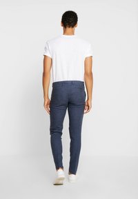 Navy tailored trousers made of textured fabric, featuring a slim fit and standard waistband, paired with a plain white t-shirt and white sneakers.
