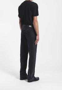 Jeans de mezclilla negra con corte recto, que cuentan con bolsillos traseros y una etiqueta en la cinturilla, acompañados de una camiseta negra de manga corta.