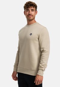 Beige Sweatshirt mit Rundhalsausschnitt und langen Ärmeln. Verfügt über ein kleines, dunkelblaues, rundes Logo auf der Brust. Weiche, glatte Textur.