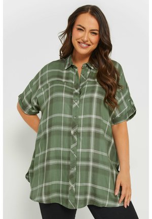 Camisa de cuadros verde en una tela ligera, con cuello tipo polo, mangas cortas arremangadas y cierre de botones. Presenta detalles en gris y blanco en el patrón.