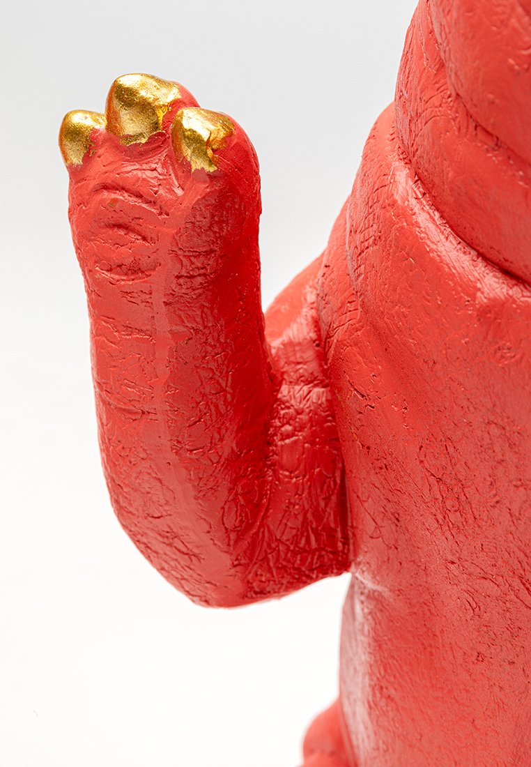 Rote Figur mit strukturiertem Oberflächen und goldenen Klaueakzenten. Das Design zeigt eine erhobene Pfote, die eine verspielte Tierform präsentiert.