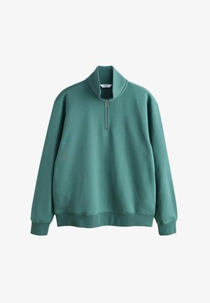 Zelena majica s četrtinsko zadrgo in dolgimi rokavi, narejena iz mehkega mešanega bombažnega materiala. Ima visok ovratnik ter rebraste manšete in rob.