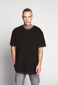 Svart oversized t-skjorte laget av bomull med kontrasterende søm detaljer. Har rund hals og korte ermer. Løs passform.