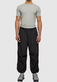 Šedé tričko s krátkým rukávem a černé volné kalhoty s elastickým pasem. Texturovaný design, šňůrky a zipy na kalhotách.