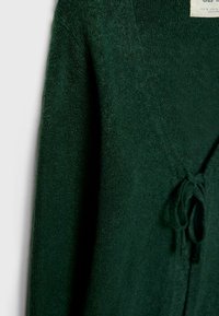 Cardigan en maille vert foncé à manches longues avec une ceinture nouée à la taille, présenté en gros plan.