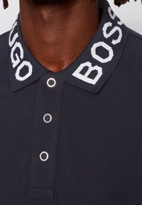 Námořnická polo košile s texturovanou tkaninou, velkým vyšitým textem "BOSS" na límci a stříbrnými kovovými knoflíky.