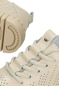 Beige kožené boty s perforovaným designem, s šněrováním a texturovanou gumovou podrážkou se specifickým vzorem.