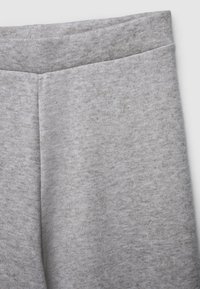 Pantaloni di tessuto grigio chiaro con un primo piano della vita e della parte superiore della coscia, che mostrano un materiale morbido e texturizzato e dettagli di cucitura.