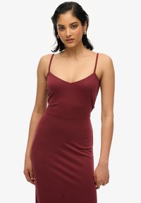 Vestido ajustado color marrón con tirantes finos y diseño de escote en V. La tela suave se ajusta al cuerpo y llega hasta el suelo con un ligero brillo.