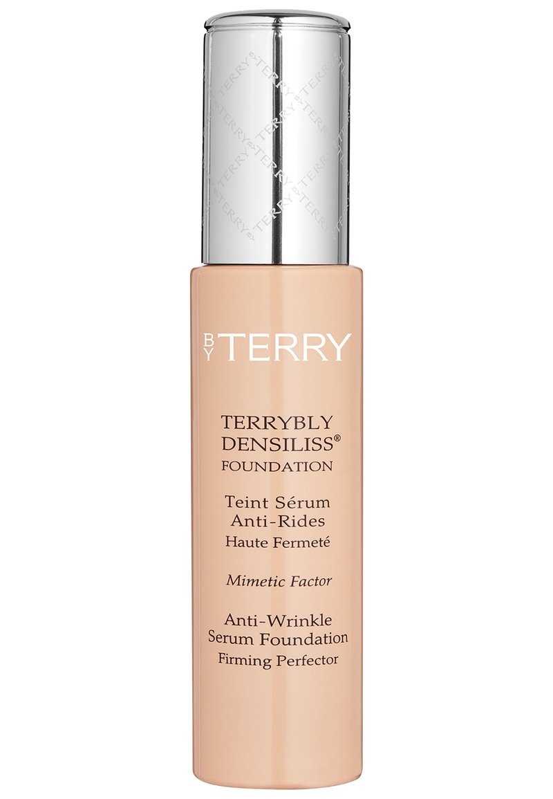 Foundation in einer klaren Glasflasche mit einem metallic-silbernen Deckel. Das Etikett hat einen beigen Hintergrund mit weißem Text, der die Produktvorteile beschreibt.