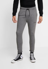 Szare dresowe spodnie w kratę houndstooth z elastycznym pasem i ściągaczem, zakończone ściągaczami na kostkach, zestawione z czarnymi sneakersami wysokimi z białym logo.