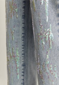 Lichtblauwe spijkerbroek met verticale en verspreide iriserende paillettenversieringen op de stof.