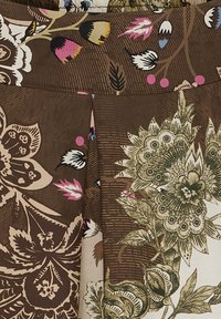 Brun tyg med intrikata blommönster i beige, vitt, rosa och grönt, med stora blommor och blad med fina linjedetaljer.