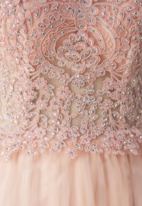 Rochie roz blush cu broderie florală complexă și mărgele. Țesătura moale din tul se desfășoară din corpul brodat, evidențiind meșteșugul detaliat.