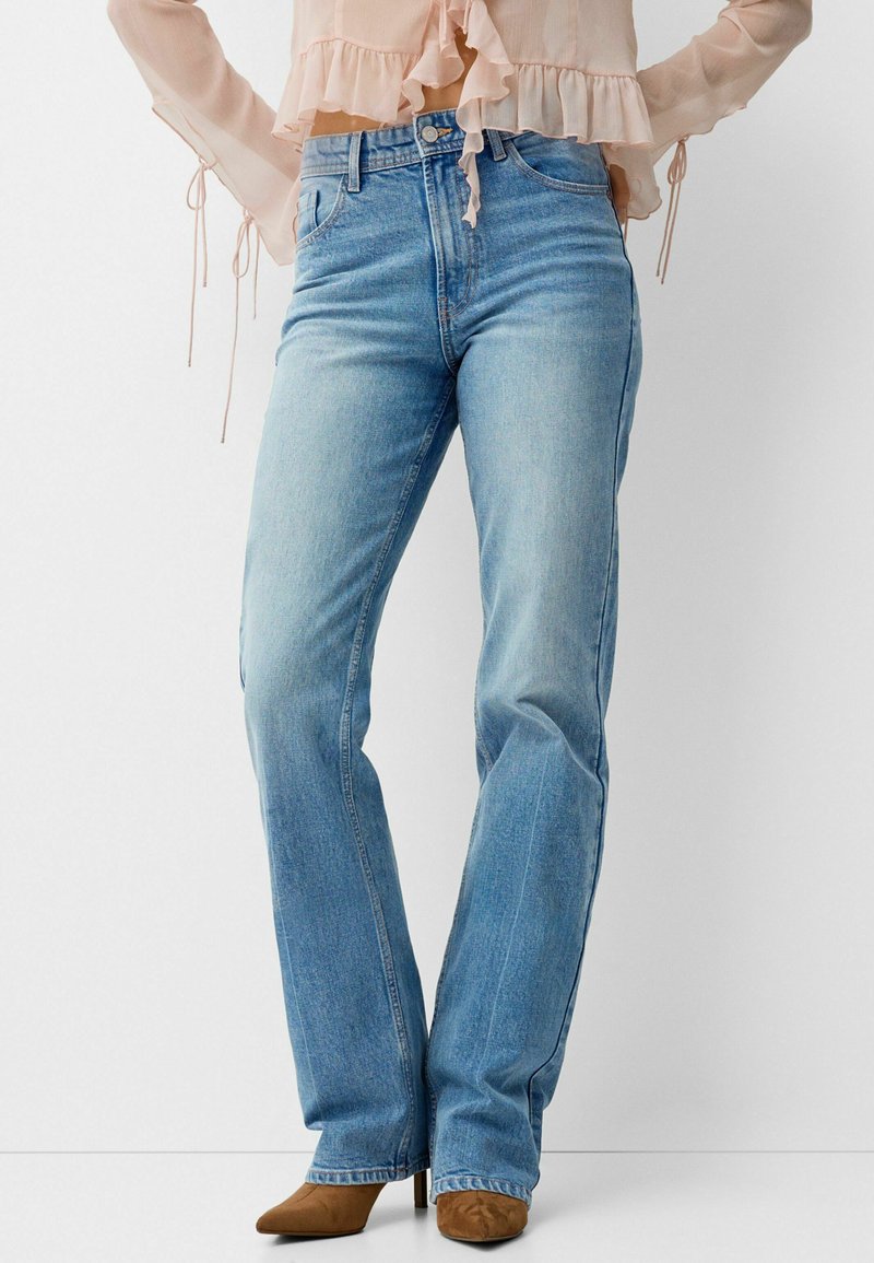 Hellblaue Jeans aus Denim mit hoher Taille, geradem Bein Design und subtiler Ausbleichung. Kombiniert mit braunen Wildlederschuhen mit Absatz.