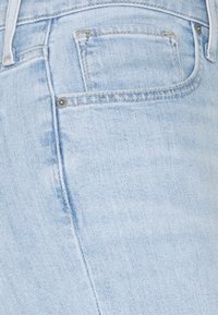 Gros plan sur un jean en denim bleu clair montrant la poche avant, la poche à monnaie et les détails de couture. Aucune personne ni autre objet visible.
