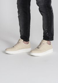 béžové semišové tenisky s bielou gumovou podrážkou, zaoblenou špičkou a šnurovaním s očkami. Nosia sa s roztrhnutými čiernymi džínsy.