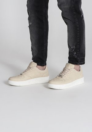 Baskets en daim beige avec semelle en caoutchouc blanc, bout rond et design à lacets avec œillets. Portées avec un jean noir déchiré.