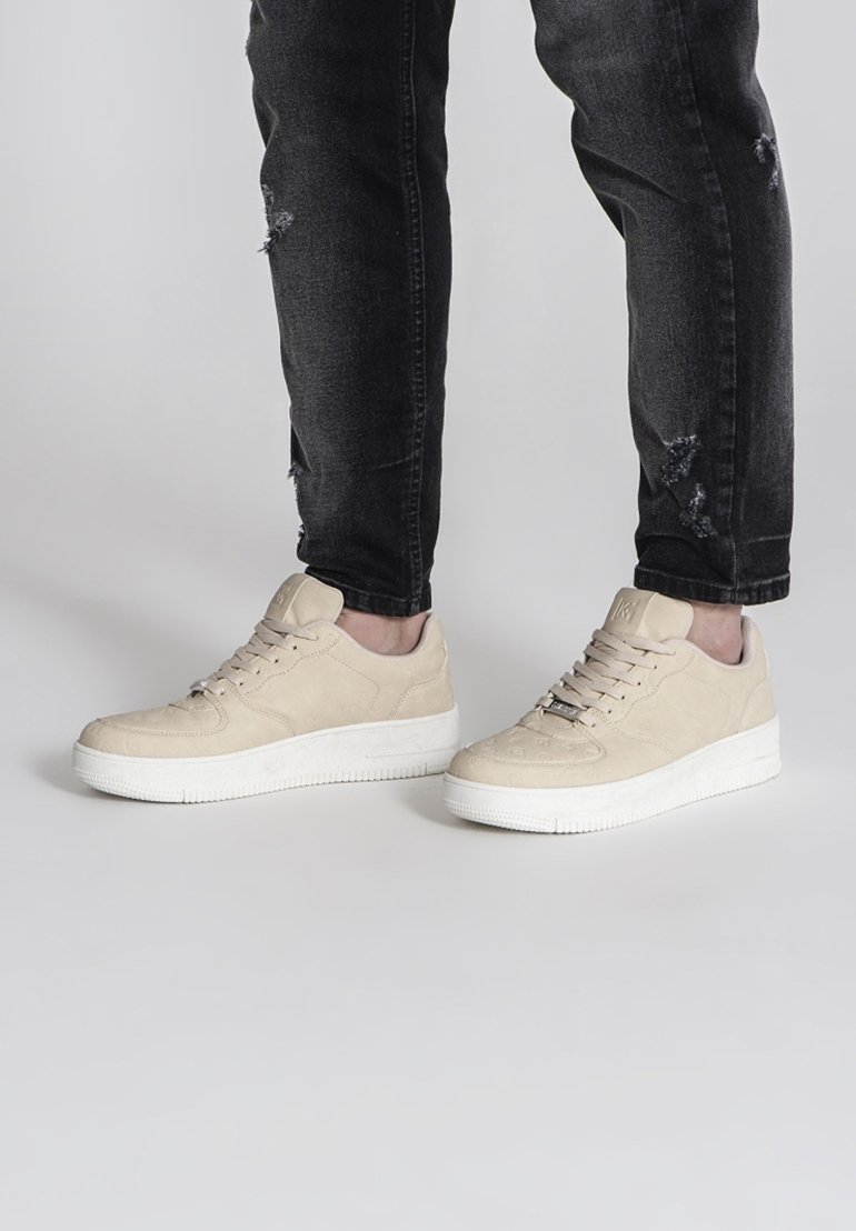 béžové semišové tenisky s bielou gumovou podrážkou, zaoblenou špičkou a šnurovaním s očkami. Nosia sa s roztrhnutými čiernymi džínsy.