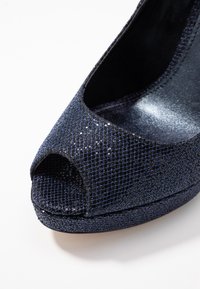 Scarpa con tacco aperto in blu scuro, con tomaia in mesh testurizzato e scintillante e interno lucido. Leggero plateau e silhouette curva.