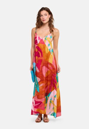 Mujer con un vestido maxi de estampado abstracto y colorido con tirantes finos, sosteniendo un bolso de mano azul y llevando sandalias marrones.