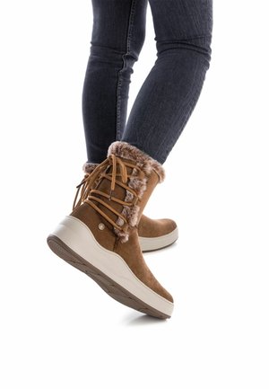 Botas de tobillo de ante marrón con puño de piel sintética, diseño de cordones y suela de plataforma blanca. Suela de goma texturizada para mayor agarre.